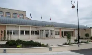 Exterior view of a building with a curved metal awning, surrounded by a landscaped area and flags.