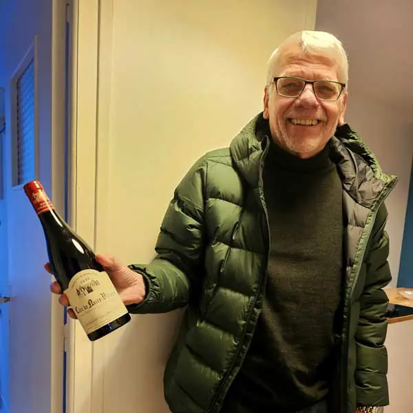 Gordon McIntosh in a green jacket and glasses holding a bottle of red wine inside a historic Seattle wine shop.