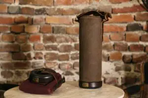 An image of a brown colored, cylindrical Vinarmour wine carrier sitting on a table against a brick background.