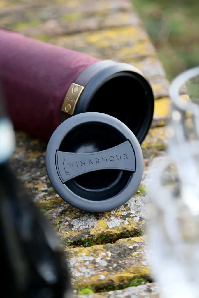 An image of a purple colored, cylindrical Vinarmour wine carrier resting on a stone wall.