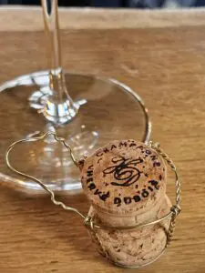 Picture of the stem of a wine glass with a champagne cork sitting on a brown wooden table.