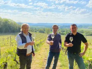 The family in charge of the Domaine de Sainte Marie raises their glasses towards the camera in a vineyard under a blue sky.