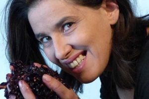 Woman smiling at the camera, holding a handful of crushed grapes in one hand