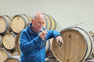 A man tasting organic Burgundy wines in a cellar filled with wooden barrels.