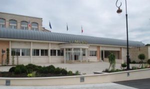 Exterior view of a building with a curved metal awning, surrounded by a landscaped area and flags.