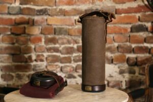 An image of a brown colored, cylindrical Vinarmour wine carrier sitting on a table against a brick background.