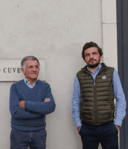 Two men stand in front of an exterior wall at Domaine Jean Michel Gaunoux-Fils.