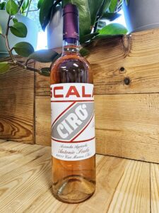 A bottle of Scala 2023 Cirò Rosato resting against a wooden background.