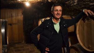A man stands in a cellar at Domaine Buisson Battault with his hand resting on a barrel.