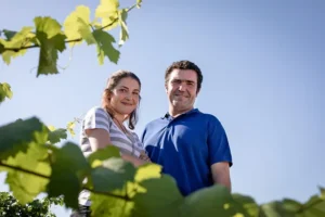 A man and woman stand amongst the vineyard of Domaine Gérard Tremblay on a clear, sunny day.