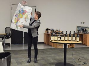 A woman holds up and displays a map while standing next to an array of wine bottles.