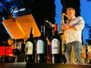 A man plays saxophone in the background while a number of Fattoria Uccelliera bottles sit in the foreground.