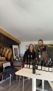 Michelle stands with Guy Amiot with bottles of wine displayed in front of them.