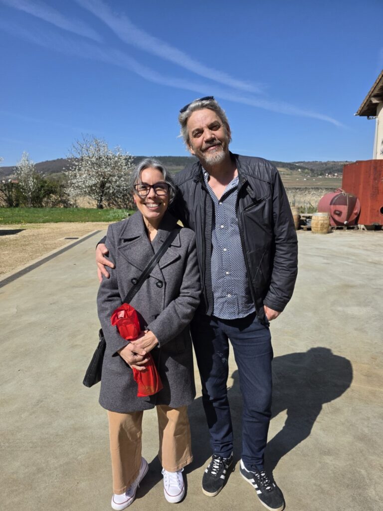 Michelle standing with a wine producer outdoors on a sunny day with blue skies.