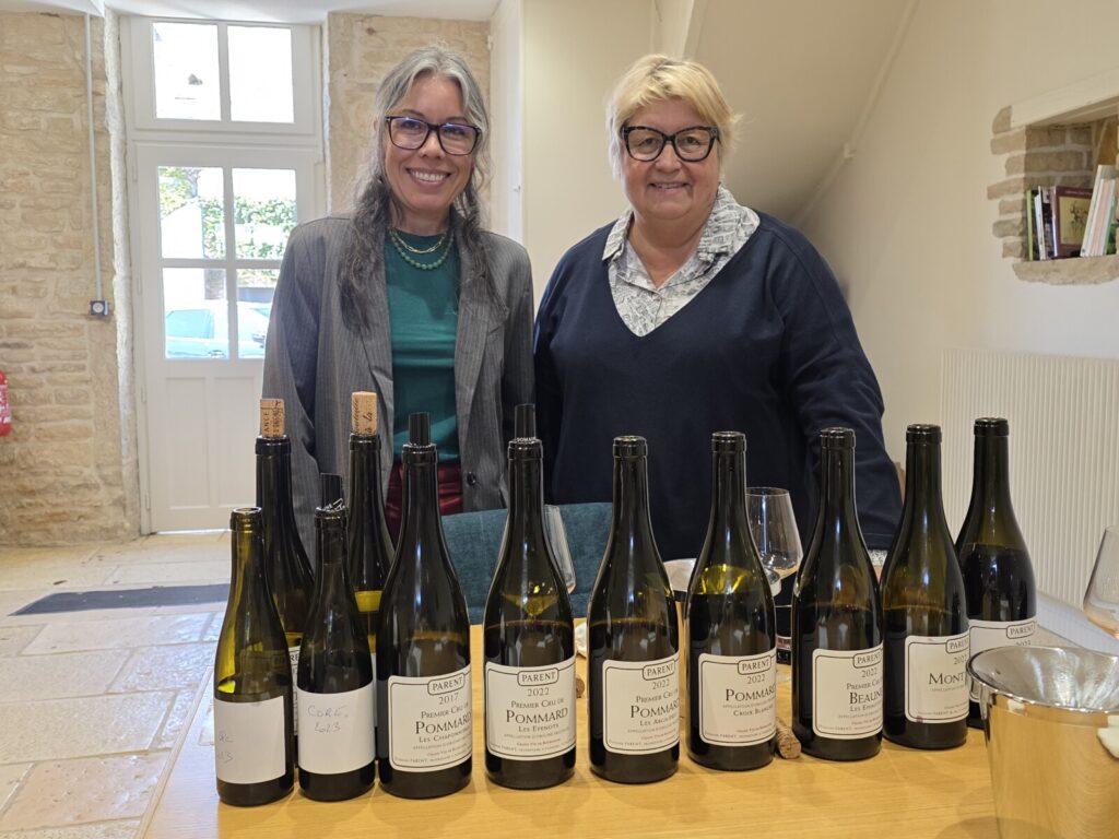 Michelle stands next to a woman in front of a table full of wine bottles.