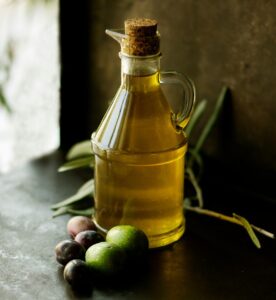 An image of olive oil on a table with olives besides it.