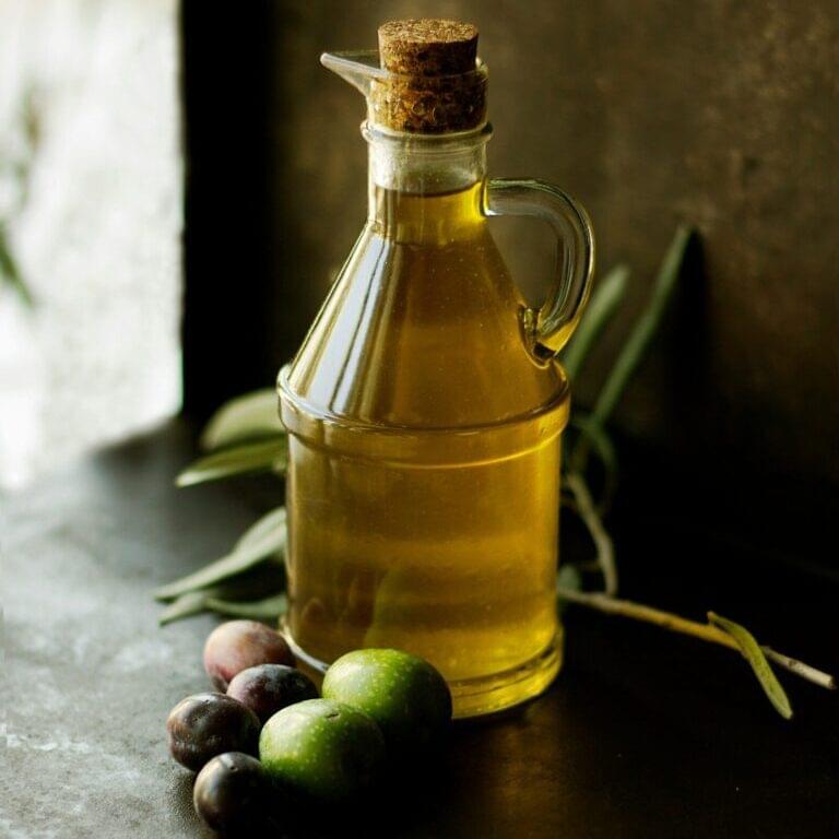 An image of olive oil on a table with olives besides it.