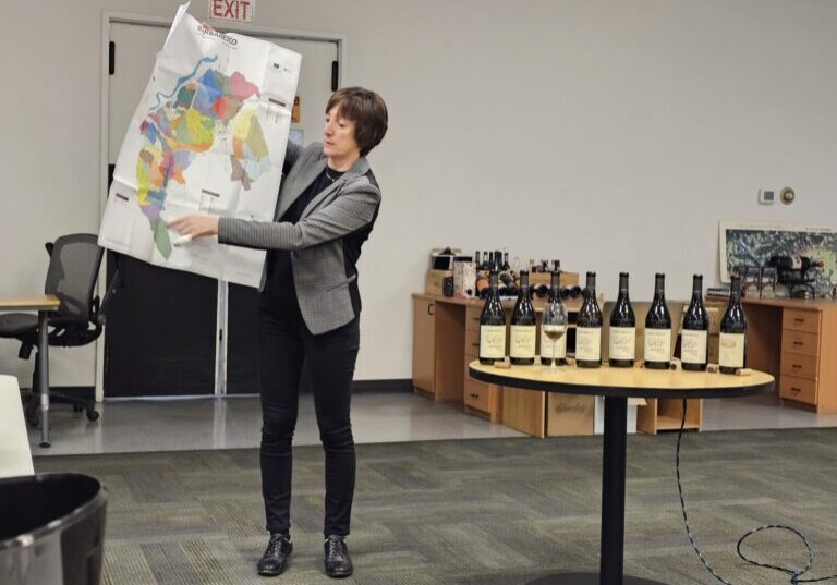 A woman holds up and displays a map while standing next to an array of wine bottles.