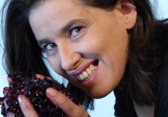 Woman smiling at the camera, holding a handful of crushed grapes in one hand