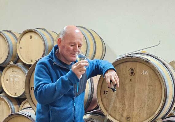 A man tasting organic Burgundy wines in a cellar filled with wooden barrels.