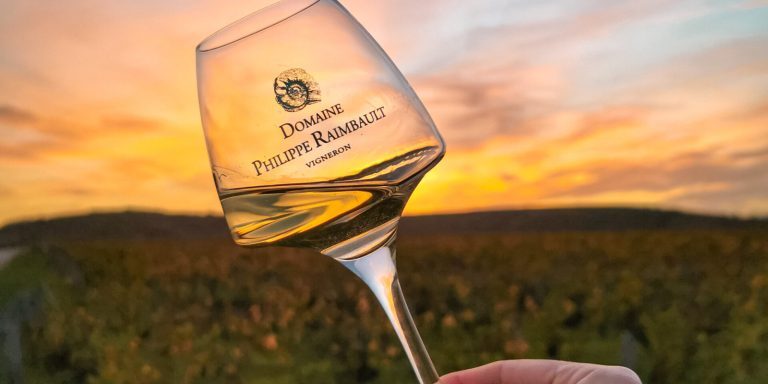 A hand holding a glass of Loire Valley wine against a sunset over vineyards.