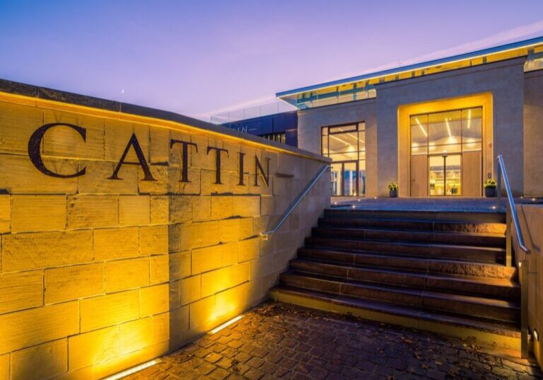 The exterior of the Joseph Cattin winery at dusk. Warm lighting illuminates the Cattin sign on the exterior wall.