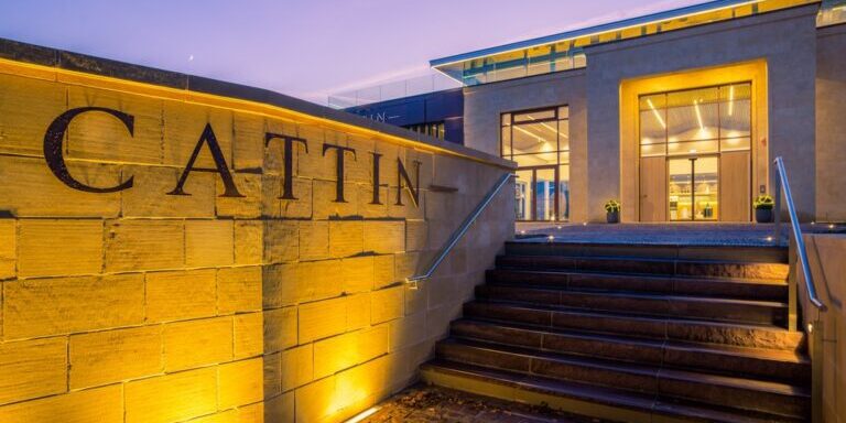 The exterior of the Joseph Cattin winery at dusk. Warm lighting illuminates the Cattin sign on the exterior wall.