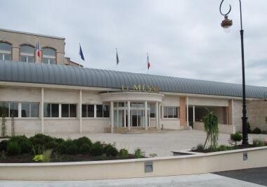 Exterior view of a building with a curved metal awning, surrounded by a landscaped area and flags.