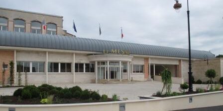 Exterior view of a building with a curved metal awning, surrounded by a landscaped area and flags.