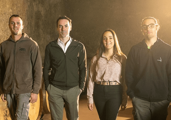 A group of 3rd generation winemarkers stands together in the Malvirà wine cellar.