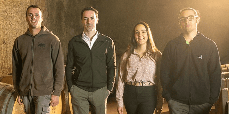 A group of 3rd generation winemarkers stands together in the Malvirà wine cellar.