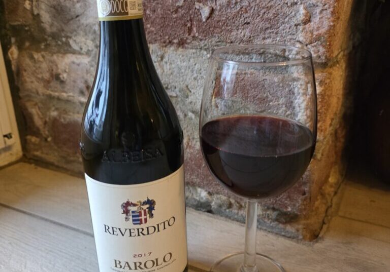 A bottle of wine next to a glass of red wine.