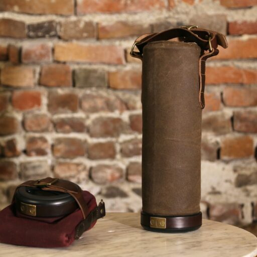 An image of a brown colored, cylindrical Vinarmour wine carrier sitting on a table against a brick background.